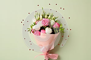 Bouquet of flowers and heart-shaped confetti on a pastel green background