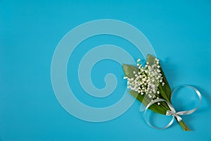 A bouquet of flowers and leaves of the may Lily of the valley Convallaria majalis with a gray bow on a light blue background.