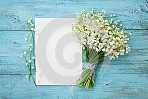 Bouquet of flowers lily of the valley and empty paper sheet on turquoise rustic table from above, beautiful vintage card, top view