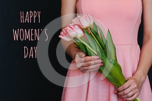 Bouquet of flowers of pink tulips in the hands of a girl. Greeting card with text Happy Women`s Day