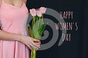 bouquet of flowers of pink tulips in the hands of a girl. Greeting card with text Happy Women& x27;s Day