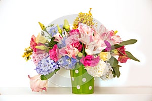 Bouquet of flowers on a shelf by the wall. Flowering branches in a bucket with a pea pattern