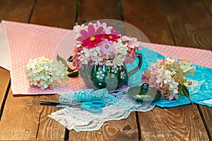 A bouquet of flowers in a teapot on a wooden table. Kitchen utensils, still life on a garden background. Plants, lace, polka dot