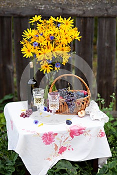Bouquet of flowers, wine, glasses and grapes against the background of an old fence