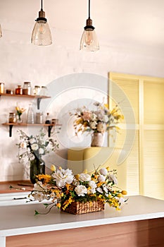 A bouquet of flowers on a wooden table. In the background, the interior of a white kitchen in the Scandinavian style