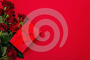 Bouquet of fresh burgundy roses and gift box on a matte red foamiran background