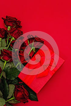 Bouquet of fresh burgundy roses and gift box on a matte red foamiran background