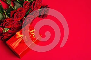 Bouquet of fresh burgundy roses and gift box on a matte red foamiran background