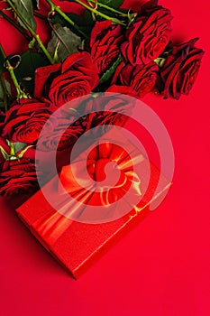 Bouquet of fresh burgundy roses and gift box on a matte red foamiran background