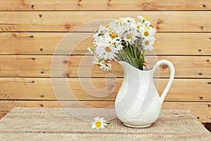 Bouquet of fresh daisies in hite jug on wooden background