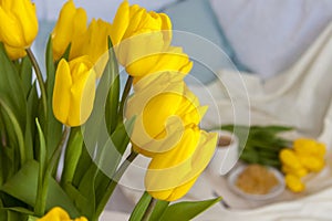 Bouquet of fresh yellow tulips close-up. Flowers in the interior on the background of the bed. Breakfast with coffee and homemade