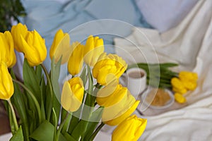 Bouquet of fresh yellow tulips close-up. Flowers in the interior on the background of the bed. Breakfast with coffee and homemade