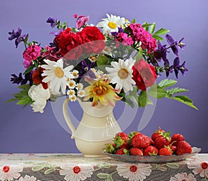 Bouquet of garden flowers in a jug and strawberries.