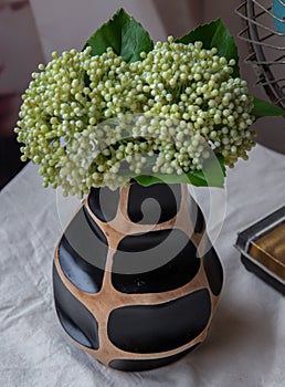 Bouquet of green in Handmade wooden vase and Vintage fan on white textured table cloth with old cement wall