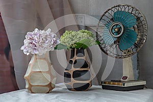 Bouquet of green and purple in Two handmade wooden vase and Vintage fan on white textured table cloth with old cement wall