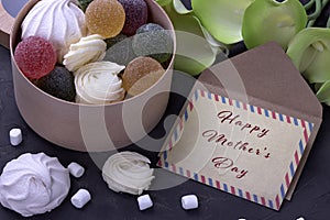 Bouquet of green yellow callas with marshmallows marmalade in a wooden round box and envelope with lettering Happy Mother`s Day on