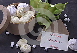 Bouquet of green yellow callas with marshmallows in a wooden round box and envelope with lettering Happy Mother`s Day on gray conc