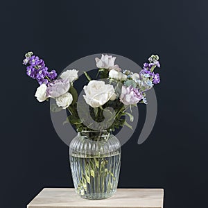 Bouquet of hackelia velutina, purple and white roses, small tea roses, matthiola incana, blue iris in glass vase opposite on black