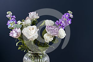 Bouquet of hackelia velutina, purple and white roses, small tea roses, matthiola incana and blue iris in glass vase .