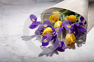 A bouquet of irises and tulips in a canvas wrap on the table.