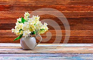 Bouquet of Jasmine flowers in a jug on a white table on a brown wooden retro background