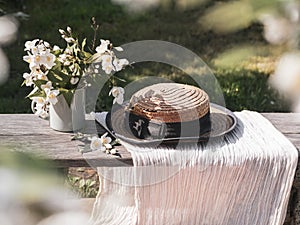 A bouquet of jasmine in a mug and a straw hat and light fabric on a wooden bench
