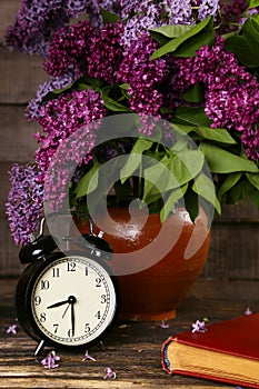 Bouquet of lilac flowers in a ceramic pot with a black alarm clock