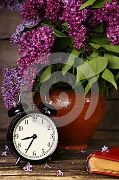 Bouquet of lilac flowers in a ceramic pot with a black alarm clock