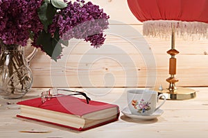 Bouquet of lilacs, book, spectacles, cup of tea and table lamp