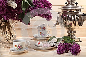 Bouquet of lilacs, samovar, cup of tea and buscuit on wooden background photo
