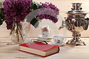 Bouquet of lilacs, samovar, cup of tea, book and spectacles
