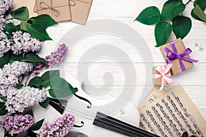 A bouquet of lilacs with violin, gift box and music sheet on a white wooden table. Top wiev with space for your text