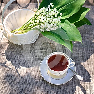 Bouquet of lilies of the valley in a beautiful white basket and a cup of tea