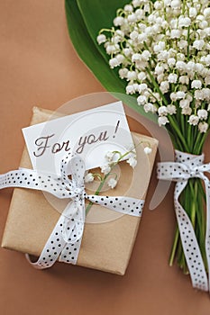 bouquet of lilies of the valley with blank gift on beige background.