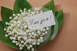 bouquet of lilies of the valley with blank gift on beige background