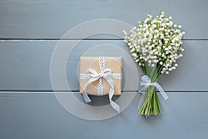 bouquet of lilies of the valley and gift on grey wooden background