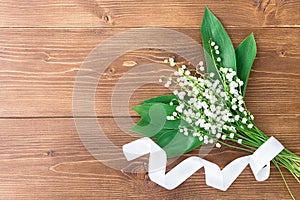 A bouquet of lilies of the valley tied with a white ribbon on a wooden background. copyspase