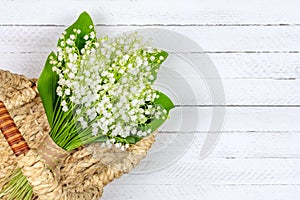 Bouquet of Lily of the valley flowers in a basket on a white wooden background with a copy space close up top view.