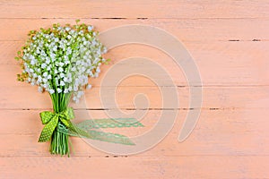 Bouquet of lily of the valley flowers with a bow and ribbon on a wooden pink background