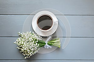 Bouquet of Lily of the valley flowers and cup of coffee on grey wooden background.