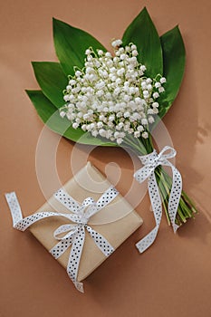 Bouquet of Lily of the valley flowers and gift on beige background.