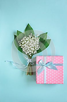 Bouquet of Lily of the valley flowers and gift on blue background.