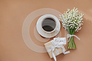 Bouquet of Lily of the valley flowers, gift and cup of coffee on beige background.