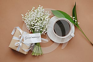 Bouquet of Lily of the valley flowers, gift and cup of coffee on beige background.