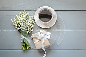 Bouquet of Lily of the valley flowers, gift and cup of coffee on grey wooden background.