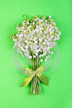 Bouquet of lily of the valley flowers with a green bow on a green background top view close up.