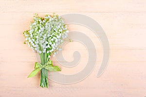 Bouquet of lily of the valley flowers with a green bow on a wooden pink background