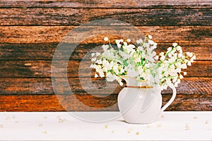 Bouquet of Lily of the valley flowers in a jug on a white wooden table on a retro grunge wall background