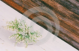 Bouquet of Lily of the valley flowers in a jug on a white wooden table on a wooden retro grunge wall background