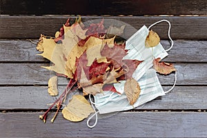 Bouquet of maple leaves and medical disposable masks on a wooden park bench. Healthcare and coronavirus concept